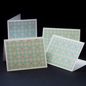 Peut inclure: Quatre cartes vierges avec un motif de diamants bleu clair et rose. Les cartes sont pliées en deux et disposées en quinconce.