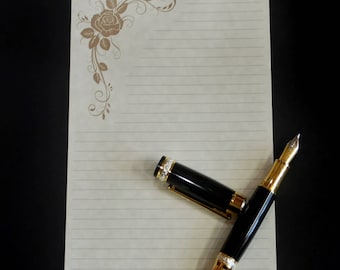 May include: A black and gold fountain pen with a decorative design on a lined sheet of paper with a floral design in the corner.