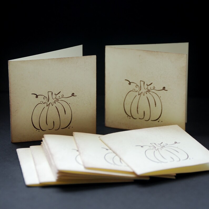 May include: A stack of blank cards with a simple line drawing of a pumpkin on each card. The cards are cream colored and have a rustic look.