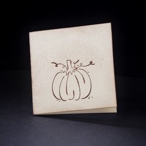 May include: A blank card with a brown line drawing of a pumpkin on it. The card is off-white and has a slightly textured surface.