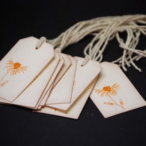 May include: A stack of blank, off-white gift tags with orange flower designs and twine attached.