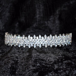 May include: A silver tiara with a floral design, set with numerous clear crystals. The tiara is displayed on a black velvet surface, showcasing its sparkle and intricate details. The tiara is a bridal or formal wear accessory.