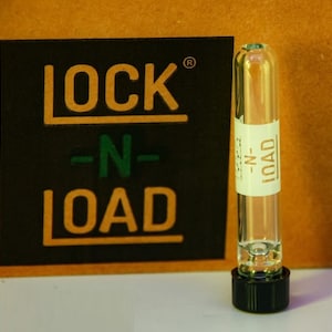 May include: A clear glass vial with a black cap. The vial has a white label with the text "LOCK-N-LOAD" printed on it.