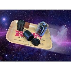 May include: A black rolling tray with the RAW logo and the text "The Natural Way to Roll".  A black and purple Time Capsule container is on the tray, along with two other black containers.