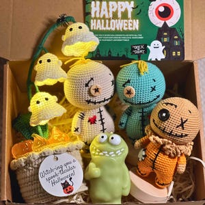 Könnte beinhalten: Eine Halloween-Geschenkbox mit drei gehäkelten Puppen, einer hellgrünen Monsterfigur und einer gehäkelten Topfpflanze mit leuchtenden Geisterlichtern. Eine Karte zeigt HAPPY HALLOWEEN und ein Anhänger Witch-ing you a spook-tacular Halloween!