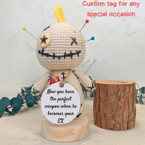 May include: A handmade voodoo doll with pins, a wooden star, and a stitched face. It has a tag that reads "Now you have the perfect weapon when he becomes your EX." A wooden log-shaped holder is next to the doll.