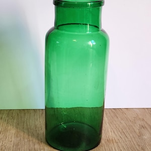Op de afbeelding: Een hoge, cilindrische groene glazen vaas met een brede opening en een licht afgeronde basis. Het transparante glas laat licht door, waardoor de levendige groene kleur wordt benadrukt. Geschikt voor het presenteren van bloemen of als decoratief stuk.