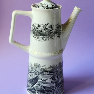 Puede incluir: Cafetera de cerámica color crema con un diseño alto y delgado. La cafetera presenta ilustraciones en blanco y negro de una escena de caza y un pájaro. Incluye una tapa a juego con un pequeño pomo y un pico largo.