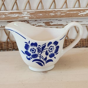 Peut inclure: Un pot à crème en céramique blanche avec un motif floral bleu. Le pot à crème a un corps arrondi et une poignée.