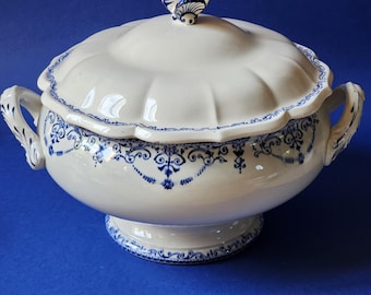 Puede incluir: Tureen de cerámica blanca con tapa, con diseños florales azules y un asa en forma de mariposa. La tureen tiene dos asas y se apoya sobre una base de pedestal. El diseño incluye detalles azules intrincados alrededor del borde y la base.