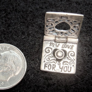 May include: A silver charm in the shape of a small book with an open heart design. The book is engraved with the words "My Love For You".