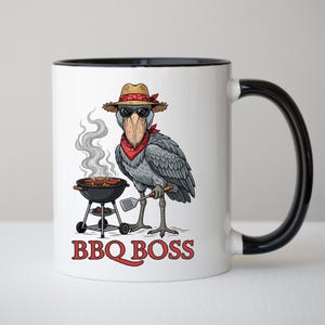 May include: White ceramic mug with a black interior and handle, featuring a cartoon Shoebill stork wearing sunglasses, a bandana, and a straw hat. The stork is grilling on a small barbecue, with the text "BBQ BOSS" in red.