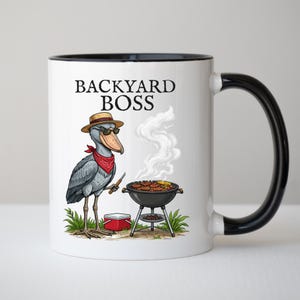 May include: White ceramic mug with a black rim and handle, featuring a cartoon illustration of a bird wearing a hat and sunglasses, grilling food. The text "BACKYARD BOSS" is printed on the mug.
