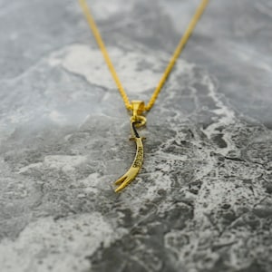 May include: A gold chain necklace with a pendant shaped like a curved sword. The sword has Arabic writing on it.