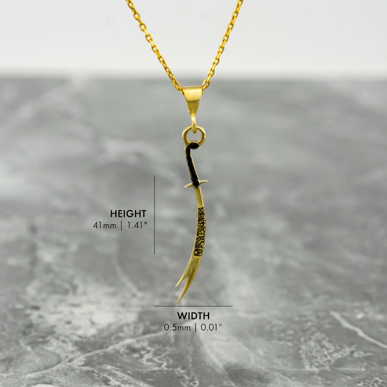 May include: Gold pendant necklace featuring a black sword with Arabic calligraphy. The pendant is 1.41 inches tall and 0.01 inches wide.
