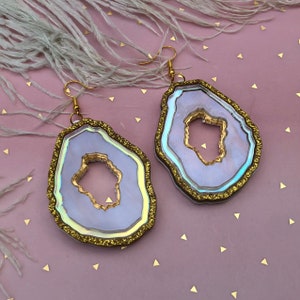 May include: A pair of iridescent agate earrings with gold glitter accents. The earrings are shaped like a geode with a large, open centre.