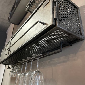 May include: A black metal wine rack with a hinged door and a wire mesh front. The rack is mounted on a wall and has a glass holder underneath.