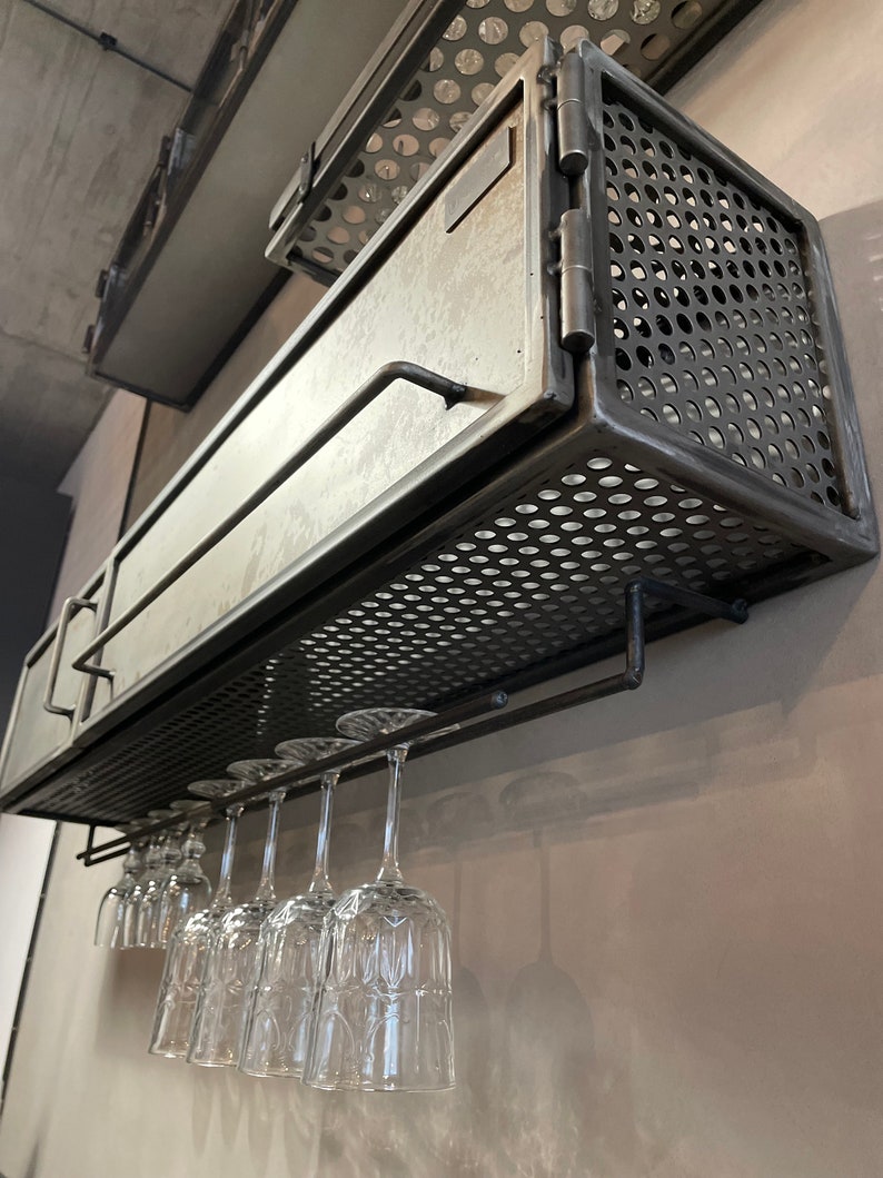 May include: A black metal wine rack with a hinged door and a wire mesh front. The rack is mounted on a wall and has a glass holder underneath.