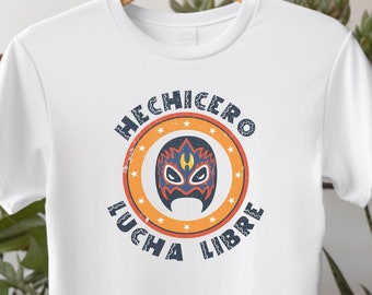 Peut inclure: T-shirt blanc avec un graphique circulaire bleu et orange qui dit "HECHICERO LUCHA LIBRE" avec un masque de lutte à l'intérieur du cercle.