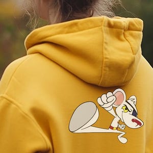 Può includere: Due persone indossano felpe con cappuccio, una blu e una gialla. La felpa gialla ha un gatto bianco dei cartoni animati con una benda nera sull'occhio sul retro.