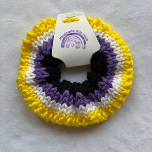May include: A yellow, white, purple and black knitted hair scrunchie with a tag that reads "Handmade With Pride".