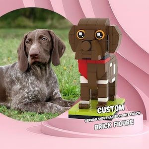 Puede incluir: Una figura de LEGO personalizada de un Braco Alemán de Pelo Corto. La figura es marrón con marcas blancas y lleva una bandana roja alrededor del cuello. La figura está de pie sobre una base verde con las palabras "CUSTOM GERMAN SHORTHAIRED POINTERBRICK BRICK FIGURE" impresas en ella.