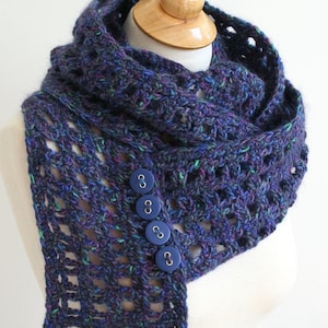 May include: A dark blue and green crocheted infinity scarf with four blue buttons. The scarf is displayed on a wooden mannequin.