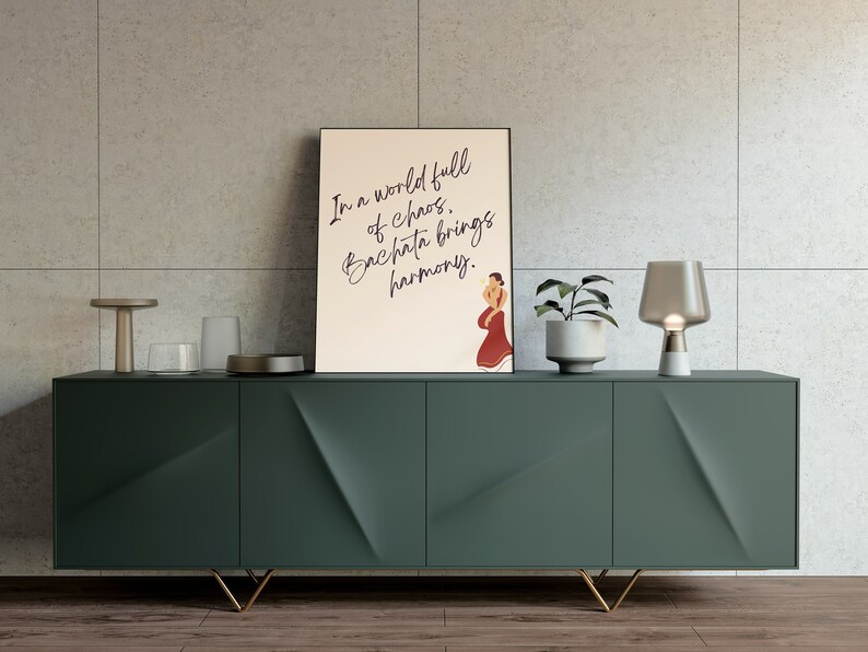 Puede incluir: Una impresi&oacute;n enmarcada con un fondo beige y texto negro que dice "En un mundo lleno de caos, la bachata trae armon&iacute;a." Una ilustraci&oacute;n estilizada de una persona bailando bachata est&aacute; en el lado derecho de la impresi&oacute;n. La impresi&oacute;n est&aacute; colgada en una pared sobre un gabinete verde oscuro con patas doradas.