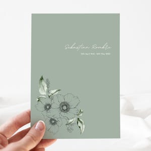 Op de afbeelding: Een saliegroene kaart met een wit bloemenontwerp en de tekst "Sebastian Roombe 12 april 1942 - 16 mei 2023".