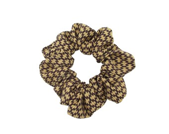 May include: A scrunchie with a brown and tan zigzag pattern. The hair accessory is circular and made of a soft fabric. This scrunchie is a stylish addition to any hairstyle.