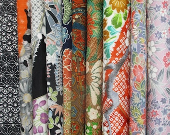 May include: A collection of vertical fabric rolls featuring diverse patterns including black and white geometric shapes, orange floral motifs, dark blue botanical prints, intricate red and gold designs, and light pink floral arrangements.