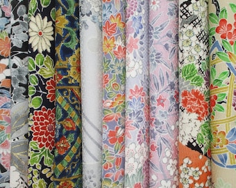 May include: A collection of vertical fabric rolls featuring diverse patterns including floral motifs, chrysanthemums, maple leaves, and geometric lattice designs in vibrant colors like red, green, blue, pink, and gold on various textured backgrounds.