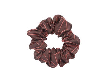 May include: A brown scrunchie with a geometric pattern in a lighter shade of brown. The fabric is gathered, creating a textured, circular shape. This hair accessory is suitable for various hairstyles.