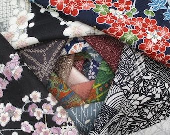 May include: A collection of folded fabric swatches arranged in a circular pattern. The textiles feature diverse patterns including red and white plum blossoms on navy, pink flowers on black, geometric grids, and intricate floral motifs in various colours.