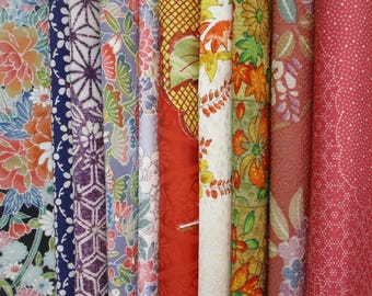 May include: A collection of vertical fabric strips featuring diverse patterns including large orange and blue floral prints, geometric purple and white designs, red textured surfaces, and intricate botanical motifs in shades of green, yellow, and pink.