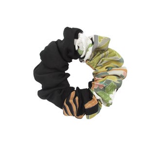May include: A black and patterned scrunchie. The scrunchie features a section of black fabric, a section with a floral pattern in green, white, and pink, and a section with a brown and black striped pattern. Hair accessory.