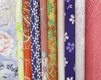 May include: A collection of rolled fabric bolts with various floral and geometric patterns. The fabrics feature colors like blue, red, yellow, and pink. Some bolts have white floral designs, while others have intricate patterns with gold accents.