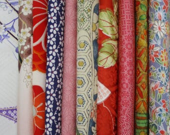 May include: A collection of vertical fabric strips featuring diverse patterns including white cherry blossoms on light pink, large red floral motifs, small white flowers on navy blue, pink geometric lines, green hexagons, red leaves, and floral prints.