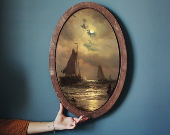 Puede incluir: Una pintura enmarcada de un paisaje marítimo con tres veleros bajo una luna llena. La pintura está en un marco ovalado de madera oscura.