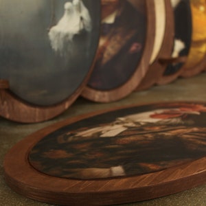 May include: A collection of oval-shaped framed artwork with various images. The frames are made of dark brown wood and have a simple design. The artwork is displayed on a brown surface.