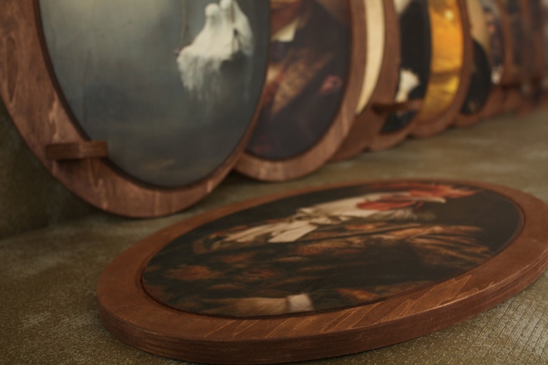 May include: A collection of oval-shaped framed artwork with various images. The frames are made of dark brown wood and have a simple design. The artwork is displayed on a brown surface.