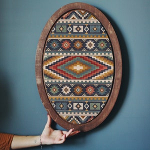 May include: A wooden oval frame with a colorful geometric pattern inside. The frame is dark brown and the pattern is a mix of red, blue, yellow, and green.
