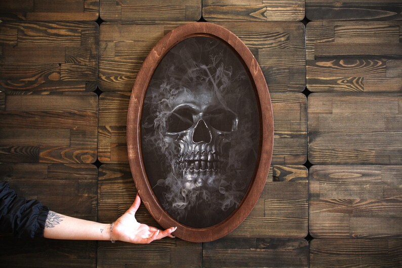 May include: A black and white skull with smoke coming out of its head, framed in a dark wood oval frame.