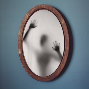 May include: A shadowy figure appears to be trapped behind a round, wooden-framed mirror.