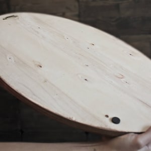 May include: The back of a round, wooden tray with a natural finish. The tray has three black rubber feet on the bottom.