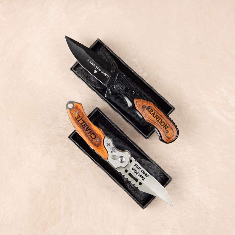 May include: Two personalized pocket knives in black boxes. One knife has a black blade with "I love you more" engraved. The other has a silver blade and the name "CHARLIE" engraved on the wooden handle. Both knives are in black boxes.