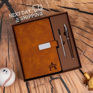 May include: A brown leather journal with a silver clasp and the name "Austin" embossed on the front, presented in a gift box with a pen and a stylus. A baseball is in the foreground. The text "NEXT DAY SHIPPING" is at the top.