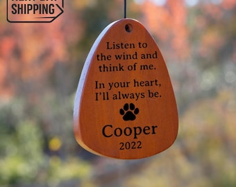 May include: A teardrop-shaped wooden wind chime ornament featuring the engraved text: Listen to the wind and think of me. In your heart, I'll always be. Below the text is a black paw print graphic, the name Cooper, and the year 2022.