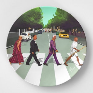 May include: A ceramic plate with a colorful illustration of four famous figures walking across a crosswalk, similar to the iconic Abbey Road album cover. The figures are walking in a line, from left to right: the Dalai Lama, Martin Luther King Jr., Nelson Mandela, and Mahatma Gandhi. The background features a street scene with trees and cars.