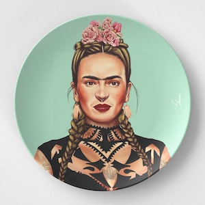 Puede incluir: Un plato de cerámica con una ilustración colorida de una mujer con una corona de flores, trenzas y tatuajes. El fondo es de color azul verdoso claro.